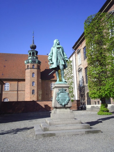 Proviantgården. Statue af Peter Griffenfeldt (1635-99), kgl. bibiotekar og ham der udfærdiger Kongeloven i 1665, den som gør Kong Frederik den 3 til enevældig konge. Loven ophæves først, da Junigrundloven træder i kraft i 1849 og som bliver fundamentet for vort nuværende demokrati.. Tøjhuset i baggrunden og Rigsarkivet til højre i billedet. Alle bygninger ligger som nabo til Christiansborg